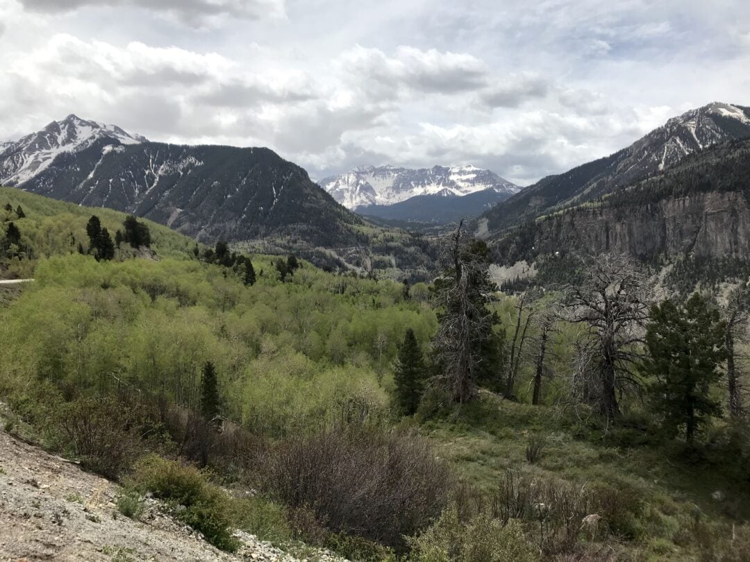 Mountains and tree dominate a rolling, green landscape.